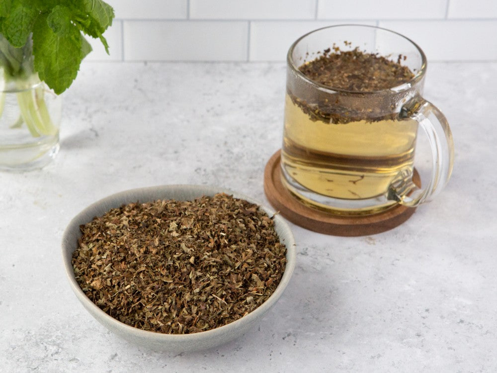 Bowl of dried herbal leaves beside a mug of herbal tea.